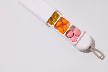 Health and medicine concept. Stylish pillbox with multi-colored vitamins, tablets, supplements on light gray background with sunny shadows top view. Organizer for multivitamins, capsules