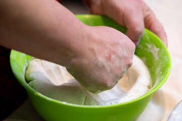 Hand kneading dough in a vibrant green bowl during a cozy kitchen session at home, blissfully creating bread in the quiet afternoon light