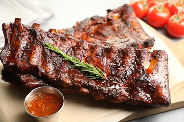 Tasty roasted pork ribs served with rosemary, tomatoes and sauce on light grey table, closeup