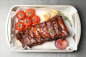 Delicious spare ribs, rosemary, baked onion and sun dried tomatoes on grey textured table, top view
