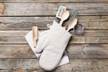Different kitchen utensils in oven mitten on wooden table, top view