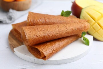 Delicious fruit leather rolls, mint and mango on white table, closeup