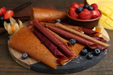Delicious fruit leather rolls and berries on wooden table, closeup