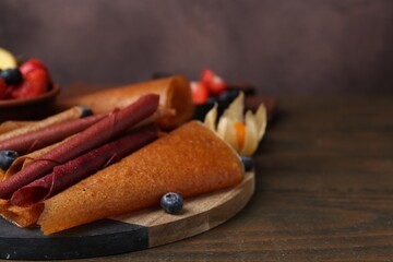 Delicious fruit leather rolls and berries on wooden table, closeup. Space for text