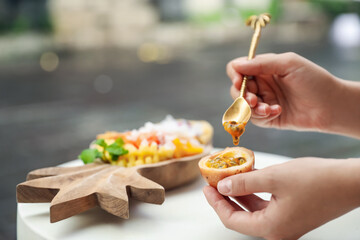 Woman eating passion fruit at table outdoors, closeup
