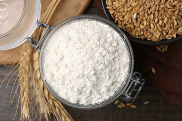 Wheat flour, grain and spikes on wooden table, flat lay