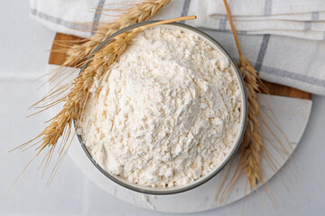 Wheat flour and spikes on white table, top view