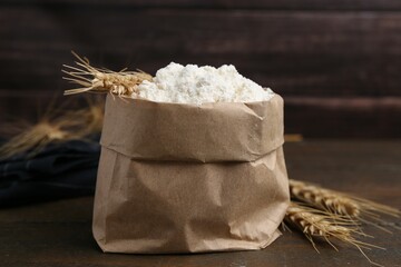 Wheat flour and spikes on wooden table, closeup