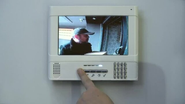 A hand interacts with a security system screen displaying a person. The screen shows a man in a cap.