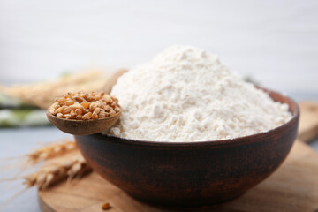 Wheat flour in bowl, grains and spikes on table, closeup
