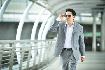 Asian businessman walking on a bridge outside office background	