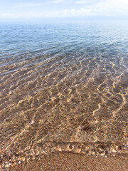 Clear lake water and pebble bottom under sun reflections