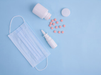 medical mask, nasal spray, pills on a blue background. View from above.
