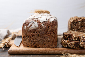 Freshly baked loaves of bread and spikes on wooden table against light grey background, closeup