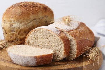 Freshly baked loaves of bread and spikes on table against light grey background, closeup
