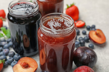 Different sweet jams in jars and ingredients on grey table, closeup