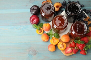 Different jams in jars and ingredients on blue wooden table, flat lay. Space for text