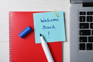 Paper note with phrase Welcome Back, laptop and stationery on white wooden table, flat lay