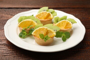 Tartlets with fruits and mint on wooden table, closeup. Delicious dessert