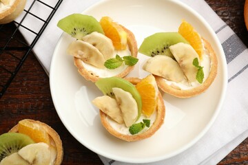 Tartlets with fruits and mint on wooden table, flat lay. Delicious dessert