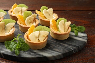 Tartlets with fruits and mint on wooden table, closeup. Delicious dessert