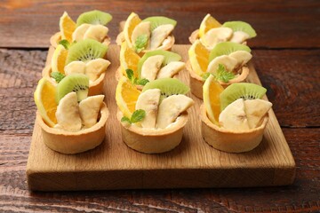 Tartlets with fruits and mint on wooden table, closeup. Delicious dessert