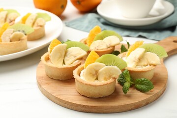 Tartlets with fruits and mint on white marble table, closeup. Delicious dessert