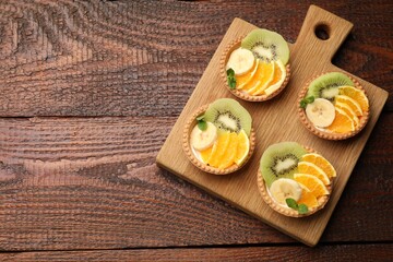 Delicious dessert. Tartlets with fruits and mint on wooden table, top view. Space for text