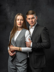 Stylish young man in formal suit standing next to charming young woman in fashionable pantsuit. Studio portrait on dark background. Concept of business fashion, and modern professional style.