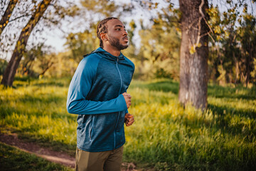 Man jogging in a wooded park during golden hour with sunlight filtering through the trees