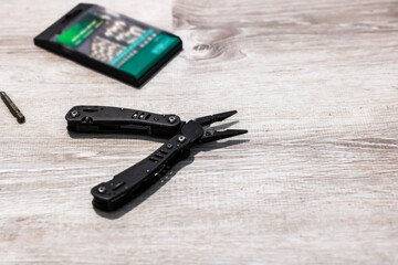 A pair of pliers sits on a wooden table next to a cell phone