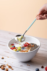 Breakfast bowl with creamy kefir, berries, kiwi, granola, and chia, with a spoonful of kefir and kiwi held by a male hand. Pastel background and wooden table. Copy space. Concept of healthy food 