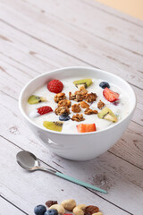 Kefir bowl with assorted fruits, granola and nuts next to metal spoon on rustic background. Fresh and realistic aesthetic. Copy space. Concept of balanced lifestyle