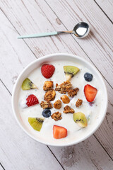Flat lay of kefir bowl with kiwi, berries, and granola on white wooden background with spoon. Minimalist style. Copy space. Concept of real food and mindful lifestyle