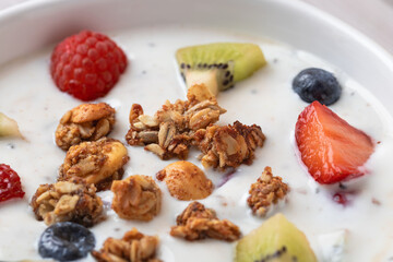 Frontal close-up of kefir with fresh fruits and granola in white bowl. Natural texture and vibrant colors. Concept of wellness, real food and probiotics
