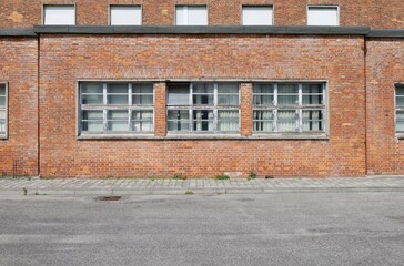 Old brick facade with  large windows downstair and a row of white shutter upstair. Tiled concrete...