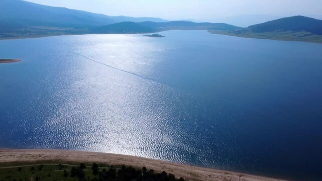 Aerial panoramic view of Batak Reservoir in Bulgaria captured by drone. Serene blue water, lush green forest and distant mountains create a peaceful, natural landscape from above.