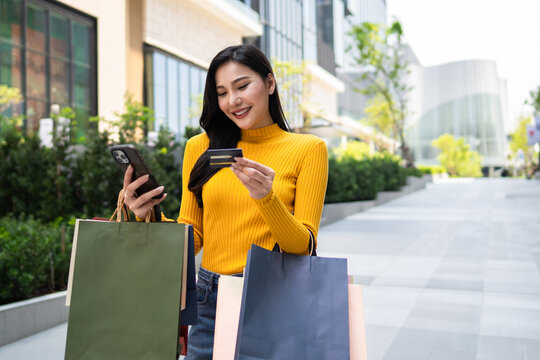 Asian woman using mobile phone shopping online outdoors in the city. 