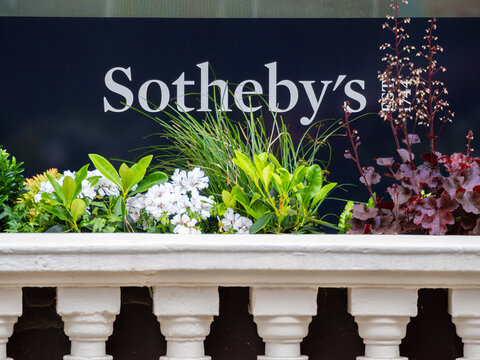 London, United Kingdom - May 26, 2025: A close-up of a Sothebys storefront sign with a dark background. Below, there is a decorative planter with various flowers and greenery.