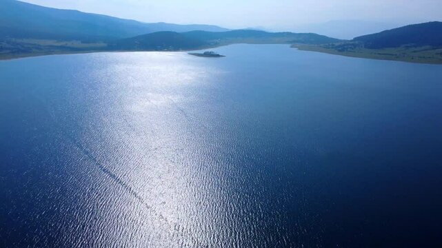 Aerial panoramic view of Batak Reservoir in Bulgaria captured by drone. Serene blue water, lush green forest and distant mountains create a peaceful, natural landscape from above.