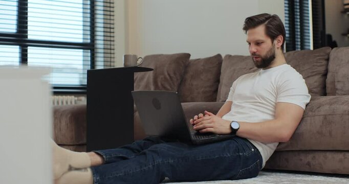 Young man sitting on the living floor room at home using laptop talk to family or friend on videoconferencing application. Virtual meeting working on laptop computer, video conference call. - Powered by Adobe
