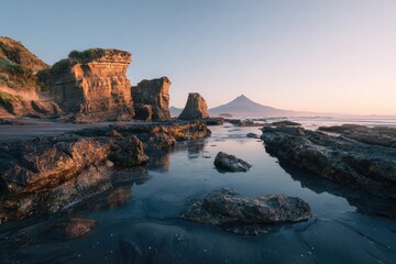 Sunrise illuminates rocky coastal formations, reflecting in calm tide pools, with a distant, hazy mountain