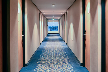 Long hallway with blue carpet and window in hotel