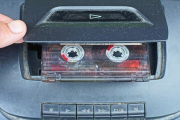 one plastic old stereo with a recording audio cassette with magnetic tape is inserted by hand into a black electric tape recorder for musical playback