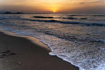 Sunrise illuminating waves crashing on alicante beach, spain