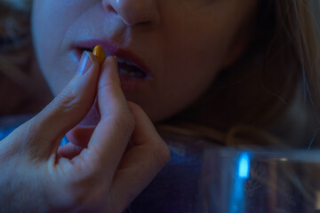 Closeup of young woman taking vitamin for treatment body strong. Woman taking yellow pill with water, closeup of hand and lips in low light, healthcare concept