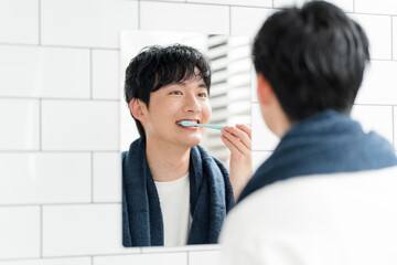 洗面所で鏡を見ながら歯を磨いている若い日本人男性