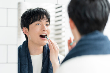 洗面所で鏡を見ながら歯を磨いている若い日本人男性
