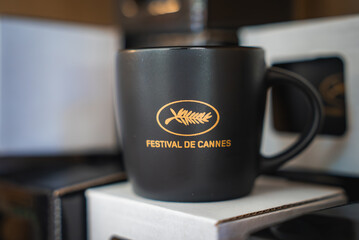 A black ceramic mug featuring the golden palm leaf logo of the Festival de Cannes, placed on a white box in a retail or souvenir setting.