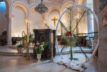 The church interior in Cannes, France, features a golden cross, dark wooden pulpit, arched columns,...
